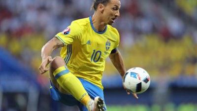 Zlatan plockar ner en fotboll från luften med ena foten. Han har gula och blå landslagskläder på sig och på tröjan syns siffran 10.