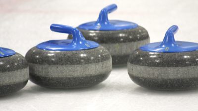 Grå curlingstenar med blå handtag som ligger på is