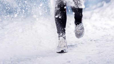 Ett par fötter och ben. De har löparskor och springer i snö som yr.