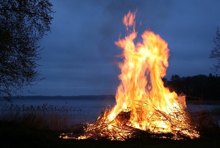En stor brasa brinner i mörker, vid en sjö.