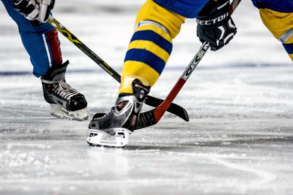 Två ishockeyspelare står på isen och tekar. Bara deras ben syns. Den ena har Sveriges färger på kläderna.