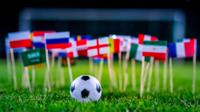 Massa små flaggor på pinnar är nedstuckna i gräset på en fotbollsplan. Framför dem ligger en liten fotboll.