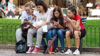 Unga tjejer som sitter på ett staket och använder sina mobiler